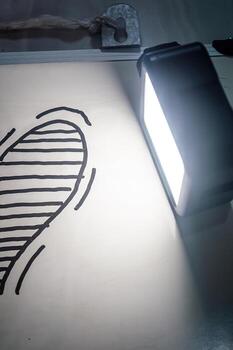Curved shaded drawing lit by LED light on white surface with metal clip symbolizing emotional depth, connection, and abstract love in a minimalist romantic concept. photo