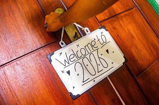 Hand holding door handle with hanging Welcome to 2020 sign featuring stars and hearts, symbolizing new year joy, hope, and fresh beginnings. photo