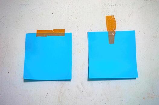 Two blank blue sticky notes taped to a textured white wall with brown tape, perfect for themes of planning, memory, minimalism, or creative workspace photo