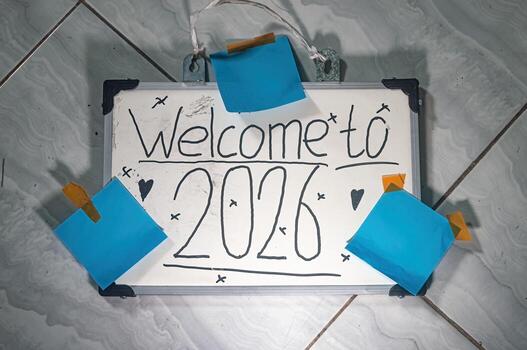 Whiteboard with Welcome to 2026 handwritten in playful style, decorated with hearts and X marks, taped with blue notes on tile floor symbolizing fresh starts and celebration. photo