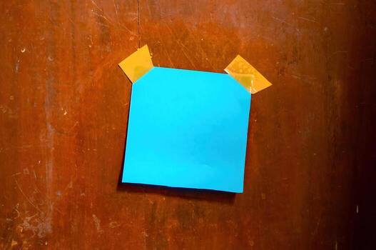 Blue sticky note taped to a worn wooden wall with yellow tape, ideal for themes of memory, DIY, rustic workspace, or creative planning aesthetics. photo