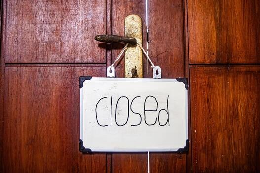 White closed sign with black corners hanging from metal door handle on wooden surface, symbolizing privacy, pause, and mindful boundaries photo