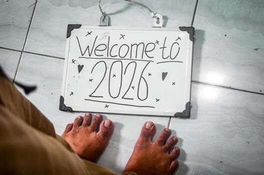 Handwritten Welcome to 2026 sign with hearts and X marks placed on tile floor near bare feet, symbolizing fresh starts, warmth, and personal reflection. photo