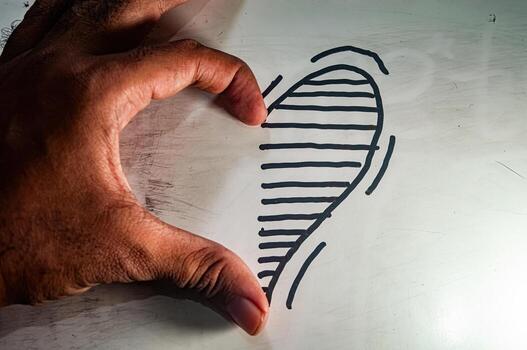 Hand forming half a heart beside a drawn half heart with black lines on white surface symbolizing love, unity, and creative connection in a minimalist romantic gesture. photo