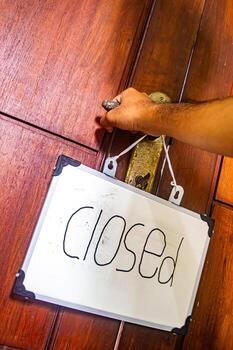 Hand gripping door handle with hanging closed sign on whiteboard, symbolizing pause, privacy, and mindful boundaries in personal or work space. photo