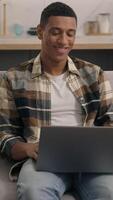 glad leende afrikansk amerikan man spelar spel med bärbar dator bläddring njuter arbetssätt på Hem manlig husägare avlägsen uppkopplad chatt social media internet webb teknologi cyberrymden kille använder sig av dator video