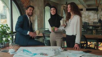 Multiracial business team discuss blueprint office renovation construction plan three architects engineers colleagues Arabian Muslim Caucasian businessman businesswomen drinking coffee happy talking video