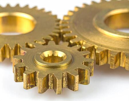 Close-up of three golden gears interlocked, set against a white background. The gears are precisely aligned and show intricate tooth patterns. Metal appears polished, showcasing a rich golden hue photo