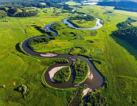 Serpentine river meanders through a vibrant green landscape. Aerial view of a winding river, creating loops and curves through a grassy plain dotted with trees. Rolling hills frame the scene photo