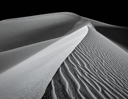 A grayscale close-up of a sand dune's crest and wind patterns photo