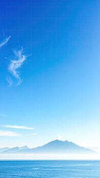 Vast, tranquil ocean meets a hazy mountain range under a vibrant blue sky photo