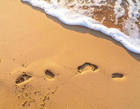 Footsteps in golden sand, a gentle wave laps the shore photo