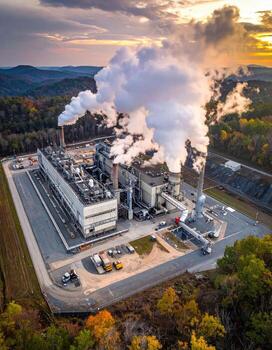 Industrial complex at sunset. Elevated aerial view of a large energy facility, with smoke plumes rising from multiple stacks against a backdrop of colorful clouds and hills photo
