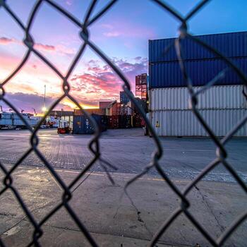 Sunset over a cargo yard, viewed through a chain link fence photo