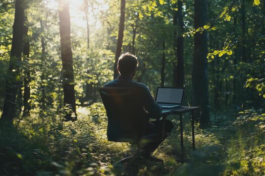 Man working on laptop in a serene forest setting during golden hour, surrounded by lush greenery and soft sunlight photo