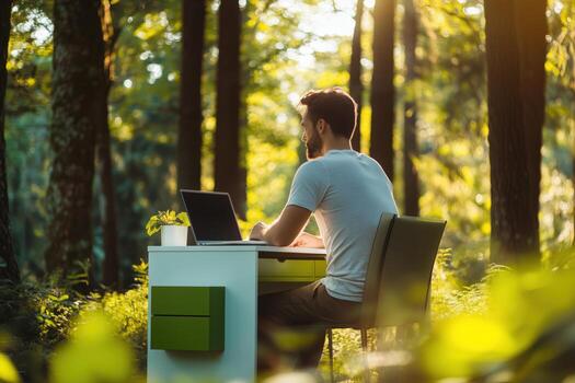 Man working on laptop at desk in lush forest during golden hour light photo