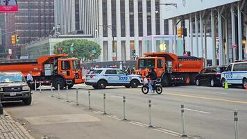 Neu York. uns. 03.03.2025 nypd Polizei Auto und Orange Lastwagen Blockierung Straße, Neu York Stadt Straße Szene mit der Verkehr Kontrolle, Radfahrer Vorbeigehen durch und Apfel Geschäft im video