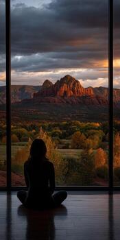 A woman sits in front of a window looking out at a view of red rock photo