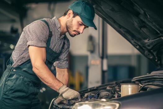 A man in overalls working on a car engine photo