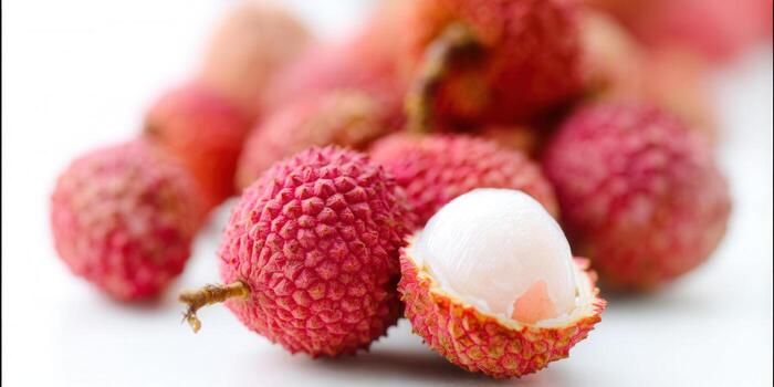 A close-up shot of a pile of fresh, red lychees, one peeled open photo