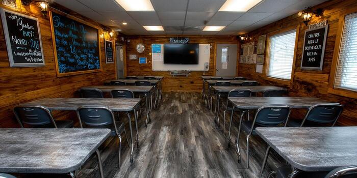 The classroom features wooden walls, a blackboard, and desks arranged for students. photo