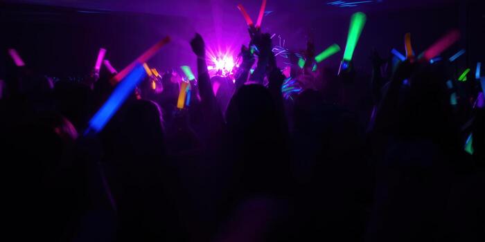Excited crowd at a concert with colorful glow sticks and vibrant lights, enjoying the music. photo