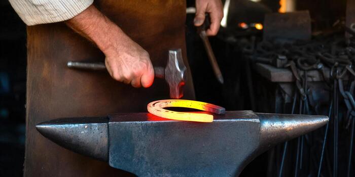 Blacksmith forges a glowing horseshoe on an anvil with a hammer in his hands. photo