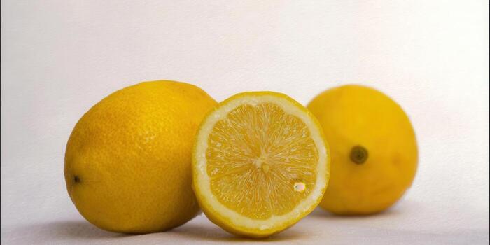 Three fresh lemons on a white surface, one cut in half. photo