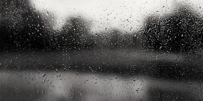 Raindrops cascade down a window, blurring the outside world into a soft, grey landscape. photo