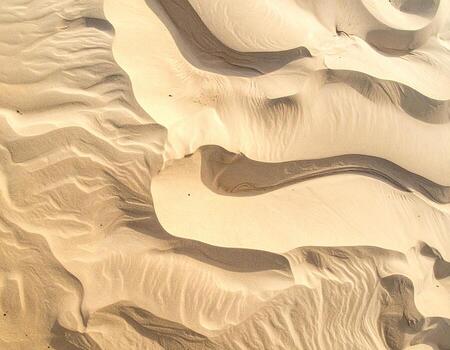 High-angle view of sculpted sand dunes. Soft, pale beige sand forms intricate, flowing patterns photo