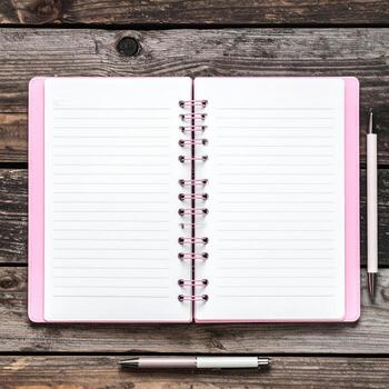 Open pink spiral-bound notebook on a wooden table, with a pen photo