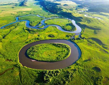 Serpentine river meanders through lush green valley. Aerial view of a winding river, creating a large loop in a grassy plain photo