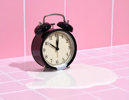 A black alarm clock sits on a pink tiled surface, with a puddle of spilled white liquid beneath it. Time stands still, suspended in a moment of dairy-inspired disruption photo