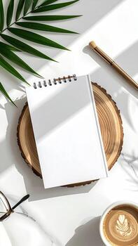 Overhead view of a blank notebook, a coffee cup, a wooden slice, and accessories on a white surface photo