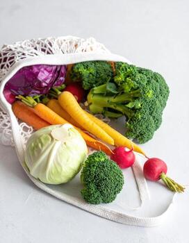 Fresh vegetables in a white mesh bag on a light gray surface photo