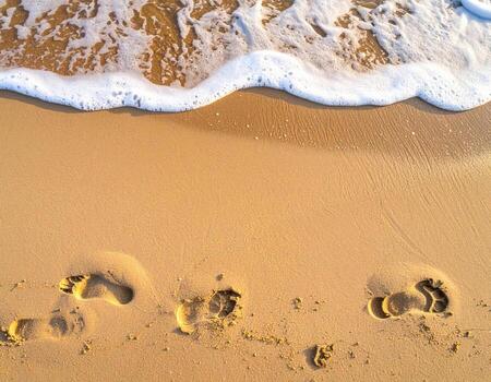 Footsteps in the golden sand, with a foamy wave edge photo
