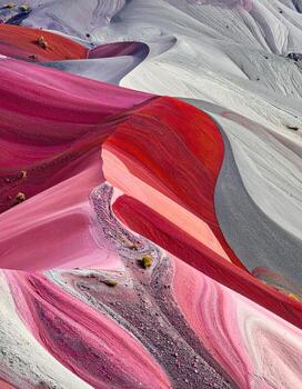 Abstract landscape of vibrant, swirling hills. Close-up view of textured geological formations in various shades of pink, red, gray, and white. Intricate patterns and curves dominate the image, with small vegetation sprinkled across the landscape photo