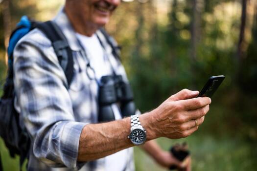 caucásico hombre en su 60s utilizando móvil aplicación para navegación mientras excursionismo en el montañas. foto