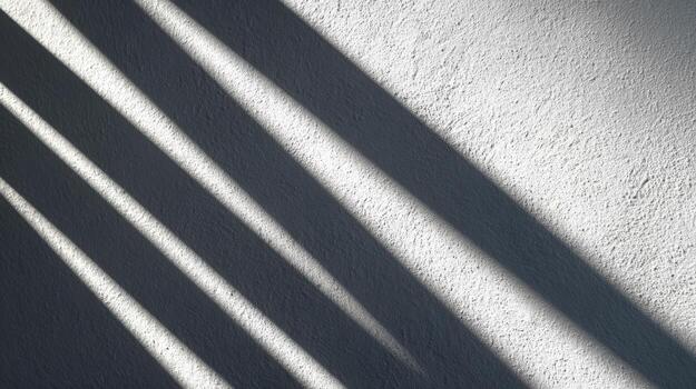Shadows of blinds on a white textured wall creating a pattern of light and dark diagonal stripes photo