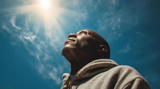 Man looking up at the sun with a blue sky and clouds in the background on a bright sunny day photo