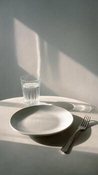 Minimalist still life featuring a glass of water, plate, and fork with strong light and shadows. photo