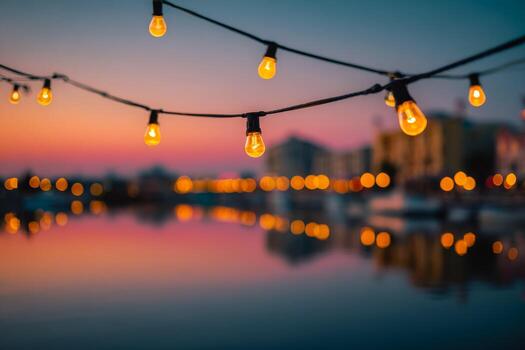 Warm glowing string lights hanging over calm waterfront during colorful sunset with softly blurred cityscape in the background creating a cozy atmosphere photo