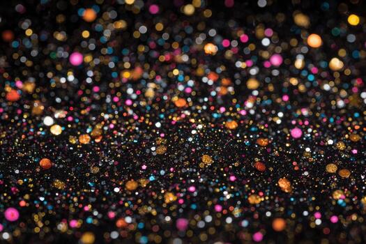 An array of colorful glitter particles in various sizes is spread across a dark surface. The vibrant hues of pink, gold, and blue sparkle against the black, creating an enchanting effect. photo
