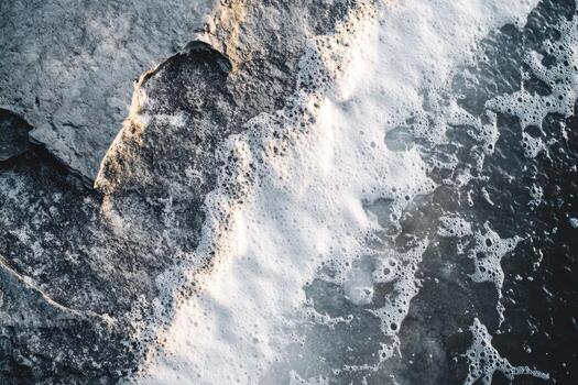 Waves crashing on rocky shore create foam in a serene coastal scene photo