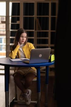 A student dedicated to learning sits at a classroom desk, utilizing a laptop and notebook to study intensively, showing concentration, discipline, and a positive attitude towards achieving photo