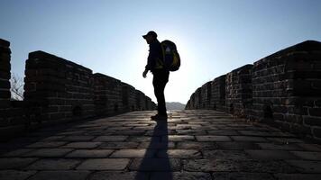 en ensam figur med en ryggsäck är bakgrundsbelyst förbi de ljus Sol. de lång skugga poäng framåt- längs de gammal sten väg, symboliserar en personlig och äventyrlig resa. video