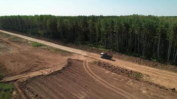 Antenne Aussicht von ein Dump LKW Fahren auf ein Wald Konstruktion Straße, treten oben Staub entlang ein Schmutz Bedienung Route während Autobahn Entwicklung. August 18, 2024, Russland video