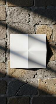 Blank white folded paper on a stone wall with shadows from tree branches photo