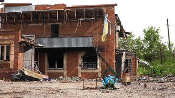 ucranio bandera ola en asta de bandera mientras guirnalda a eso base honores esos quien murió con destruido edificio a antecedentes en Járkov oblast cada detalle capturas dolor, valor y inflexible Resiliencia video