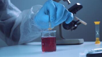 avvicinamento di mano di medico lavoratore nel protettivo completo da uomo e guanti prende campioni di rosso liquido con pipetta. scienziati Lavorando nel laboratorio. rosso chimico sostanza nel bicchiere conico borraccia con pipetta video